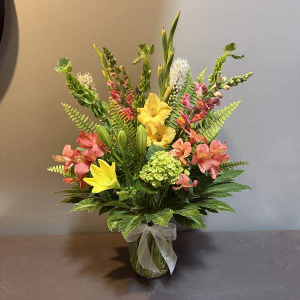 Mixed bouquet of yellow and pink flowers in a glass vase with a ribbon