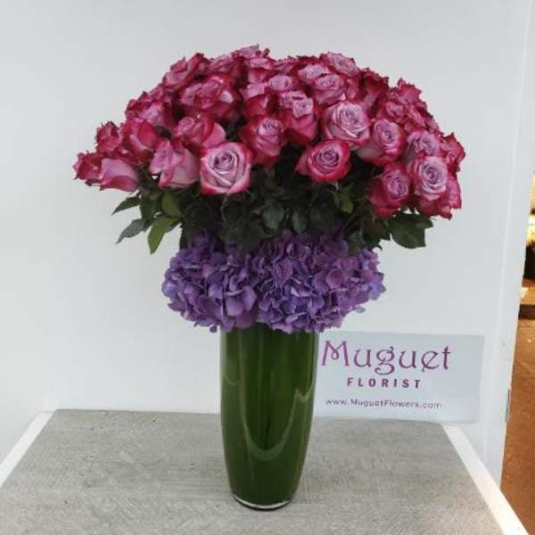 Pink roses and purple hydrangeas arranged in a tall green vase