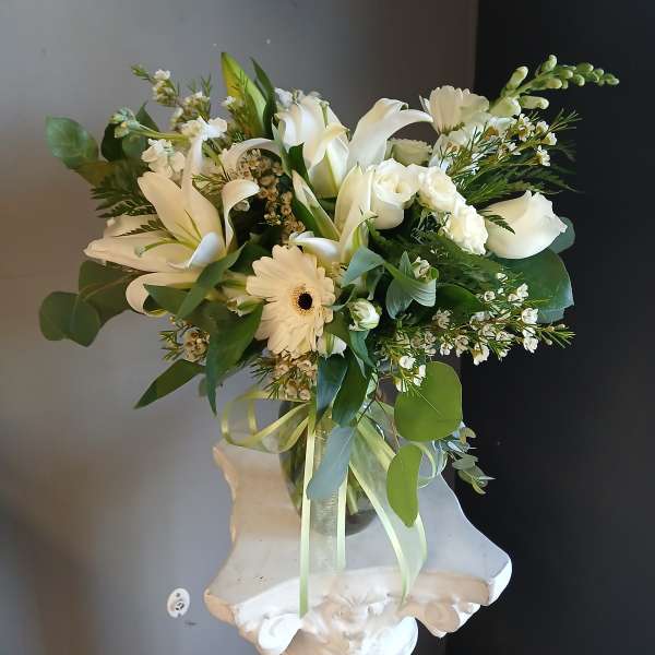 White floral bouquet with lilies, roses, and a gerbera daisy in a glass vase