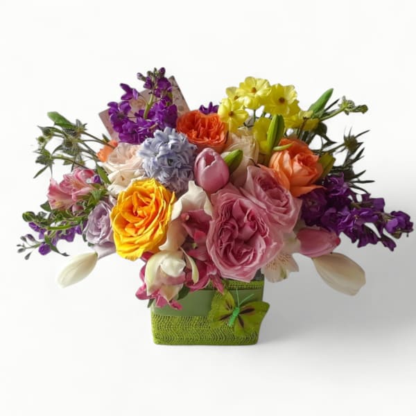 Colorful mixed arrangement of roses, tulips, and other blooms in a green cube vase with a butterfly accent