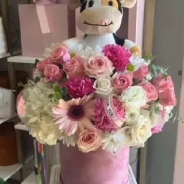 Pink flower bouquet with a plush cow topper in a pink hatbox