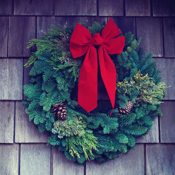 Evergreen wreath with a red bow and pinecones on a shingled wall