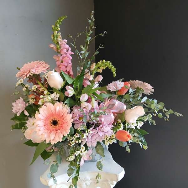 Pink and white mixed flower arrangement in a white pedestal vase