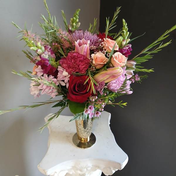 Mixed bouquet of roses, lilies, and purple blooms in a gold vase