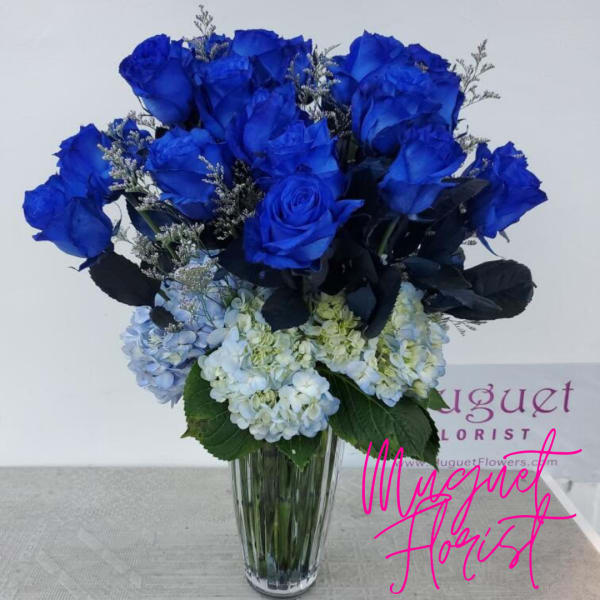 Blue roses and pale hydrangeas arranged in a clear glass vase