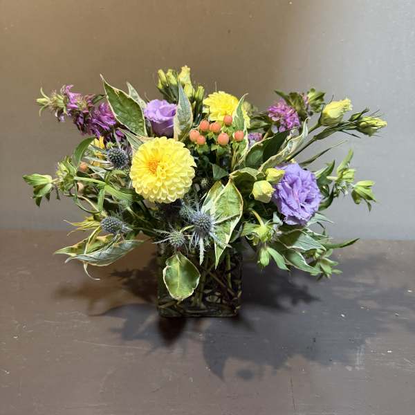 Mixed bouquet in a square glass vase with yellow, purple, and pink blooms