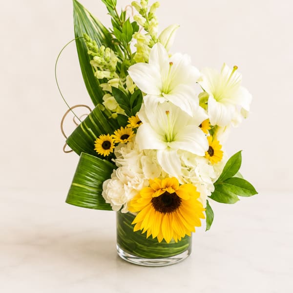 White lilies and yellow sunflowers in a glass vase