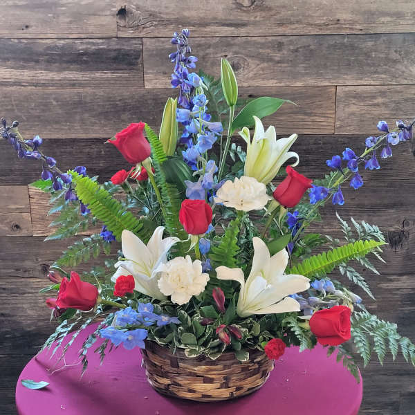 Basket arrangement with red roses, white lilies, and blue flowers