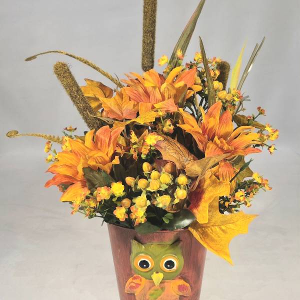 Orange floral arrangement in a painted owl pot with autumn leaves