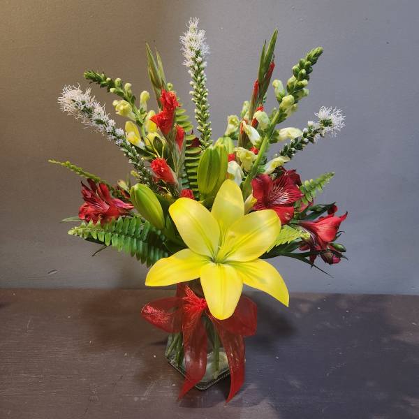 Yellow lily arrangement with red flowers in a glass vase