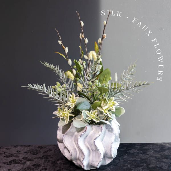 Silk floral arrangement in a wavy white vase with tall branches