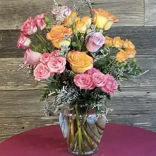 Arrangement of pink, orange, and yellow roses with white filler flowers in a clear glass vase.