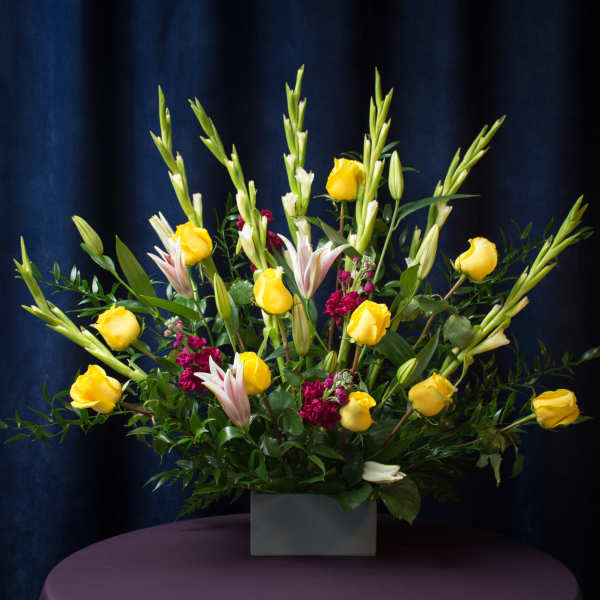 Yellow roses and lilies arranged in a square vase