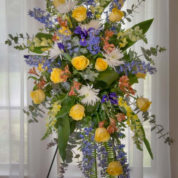 Tall floral spray with yellow roses, blue flowers, and white blooms on a stand