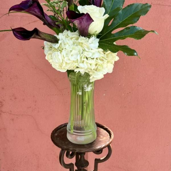 White hydrangeas and purple calla lilies in a clear glass vase