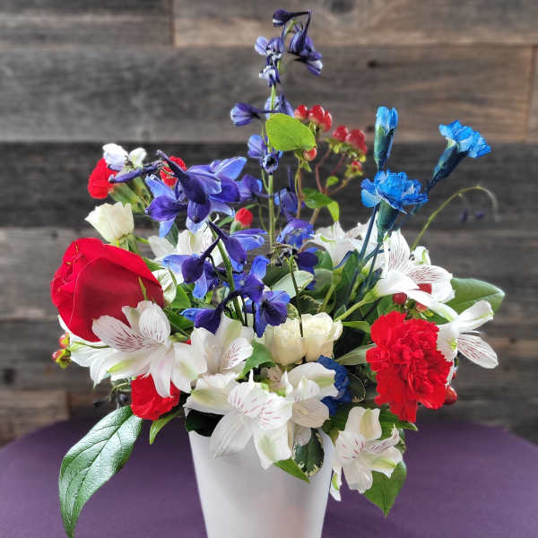 Mixed bouquet of red, white, and blue flowers in a white vase