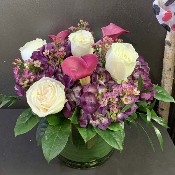 Bouquet of white roses, pink calla lilies, and purple hydrangeas in a glass vase