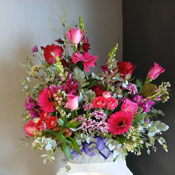 Mixed pink and red flower arrangement in a white vase with a purple ribbon