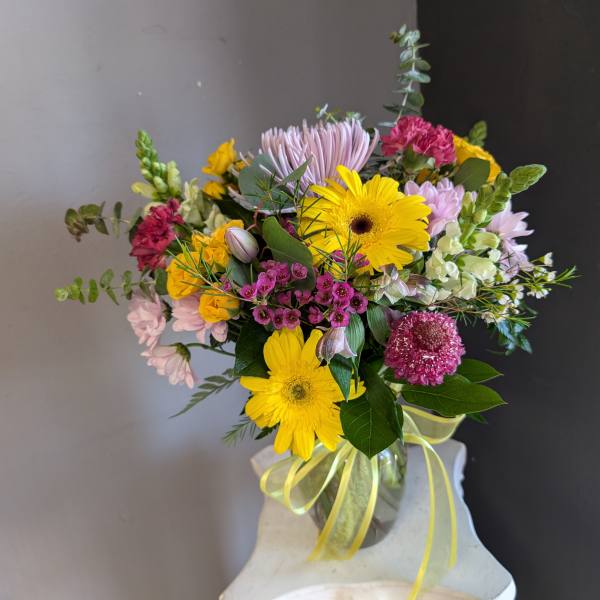 Mixed bouquet of yellow gerbera daisies and pink flowers in a glass vase