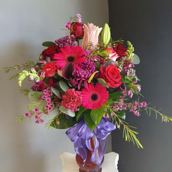 Mixed bouquet of pink and red flowers in a glass vase with a purple ribbon