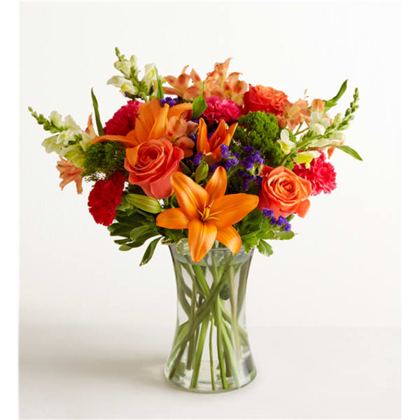 Orange lilies and roses in a clear glass vase