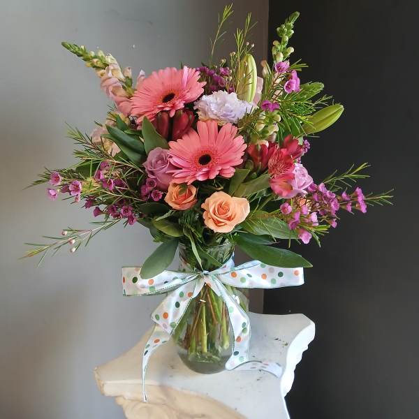 Mixed bouquet of pink and peach flowers in a glass vase with a polka-dot ribbon