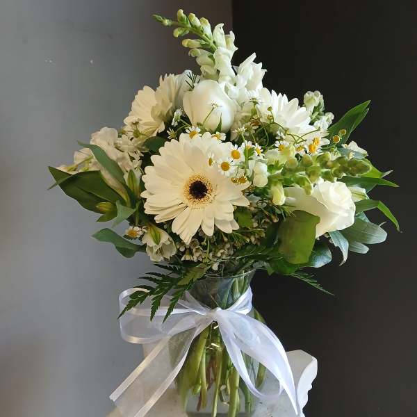 White bouquet with gerbera daisies, snapdragons, and a ribbon-tied glass vase