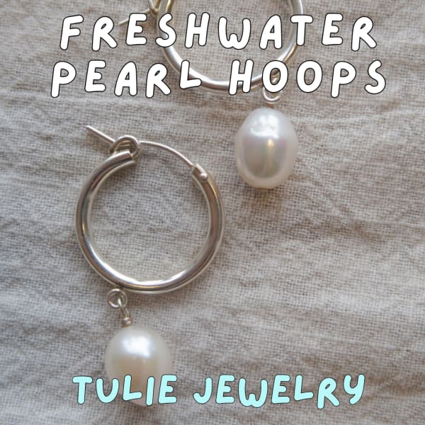 Silver hoop earrings with dangling pearls on a textured fabric background