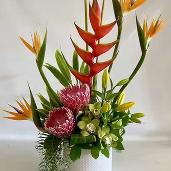 Tropical flower arrangement with red and orange blooms in a white vase