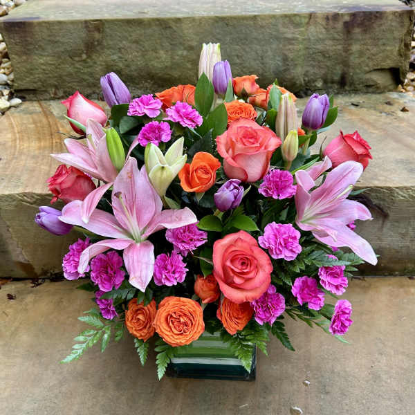 Mixed bouquet of pink lilies, roses, and orange blooms in a glass vase