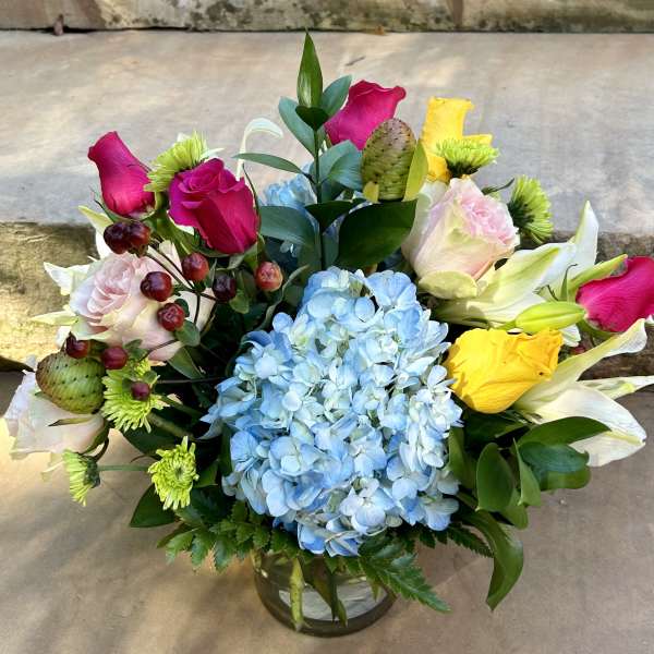 Mixed bouquet with blue hydrangea, pink roses, and yellow lilies in a glass vase