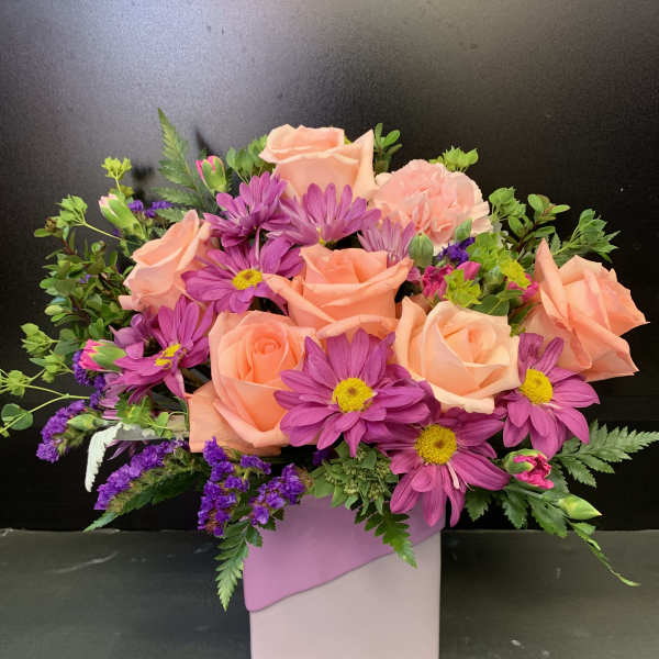 Peach roses and purple daisies in a pink square vase