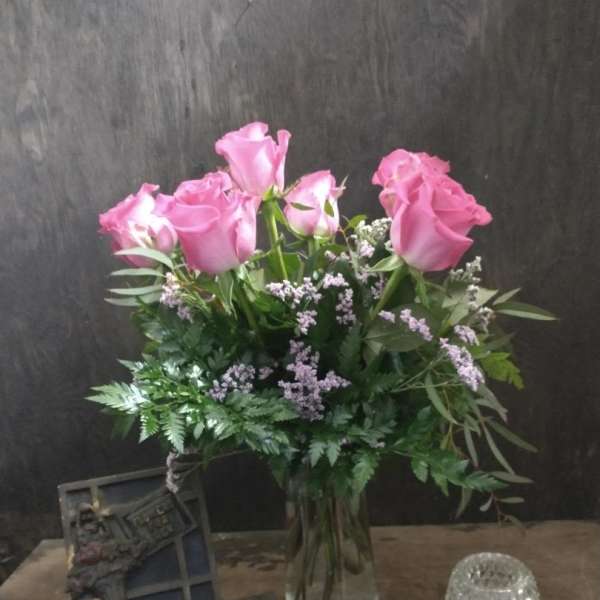 Pink roses in a glass vase with greenery and small filler flowers