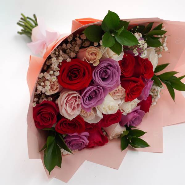 Bouquet of red, pink, and lavender roses wrapped in pale pink paper