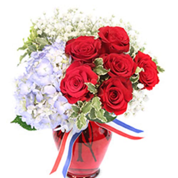 Red roses and pale blue flowers in a red glass vase with ribbon