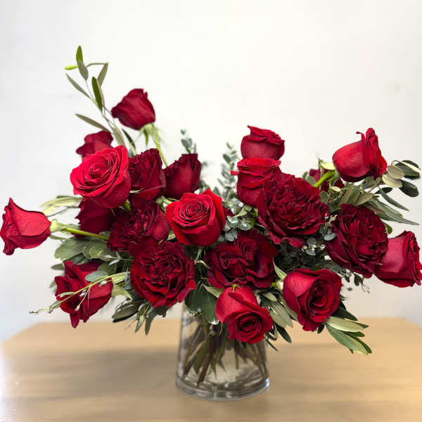 Red roses arranged in a clear glass vase with greenery