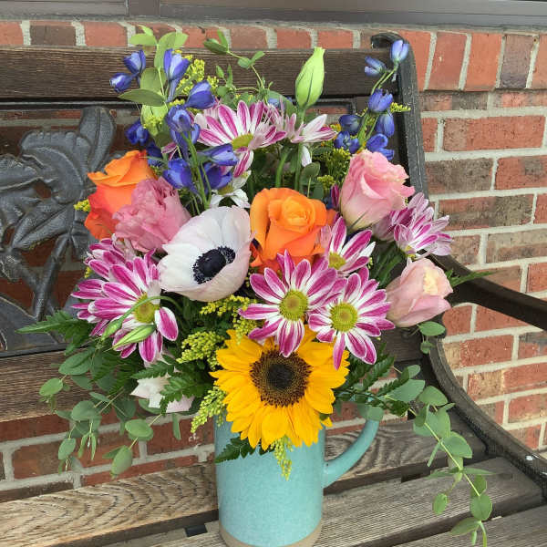 Mixed bouquet in a blue pitcher with sunflowers, roses, and daisies