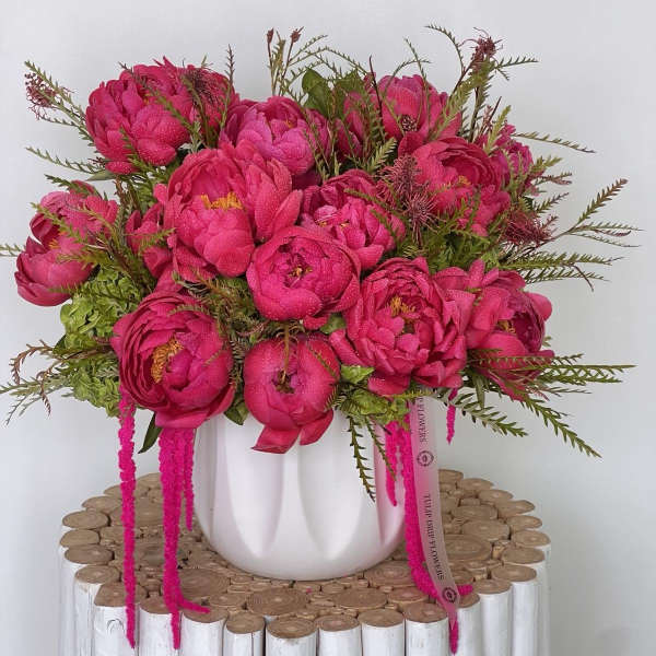 Bright pink bouquet in a white vase on a wooden stand