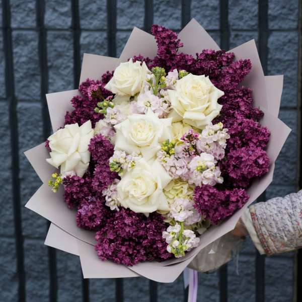 Bouquet of white roses and purple lilacs wrapped in pale paper