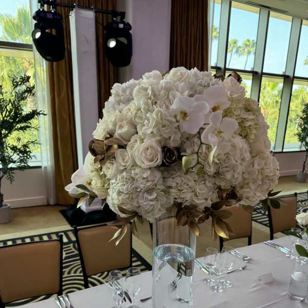 Large white floral centerpiece in a tall glass vase on a set dining table