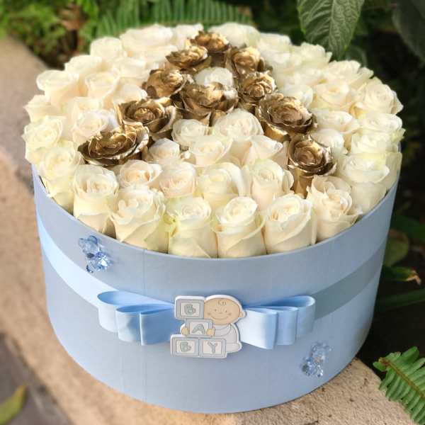 Round box of cream and gold roses with a blue ribbon and baby decoration