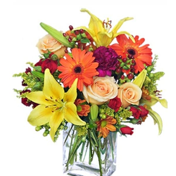 Mixed bouquet in a clear glass vase with lilies, roses, and orange daisies