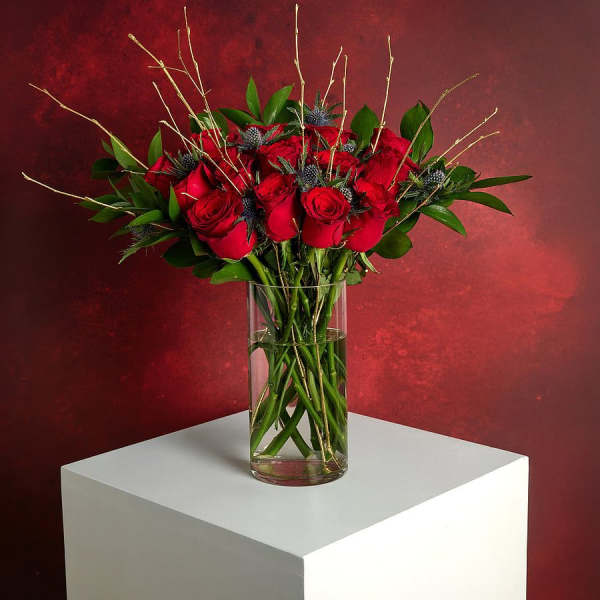 Red roses arranged in a clear glass vase with greenery and twig accents
