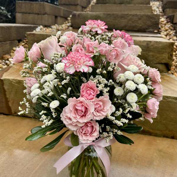 Pink roses and carnations in a glass vase with a pink ribbon