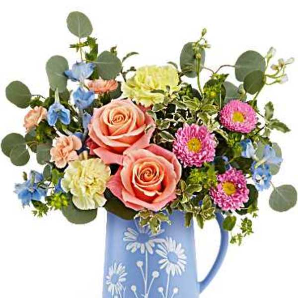Mixed bouquet of roses, carnations, and daisies in a blue pitcher vase