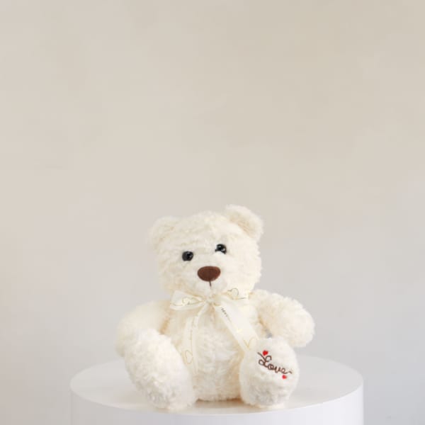 Cream teddy bear with a ribbon sitting on a white pedestal