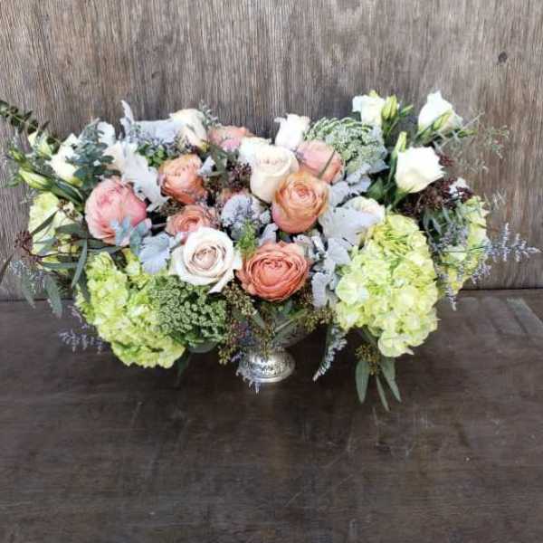 Low floral centerpiece with peach and white roses and pale green hydrangeas in a silver vase