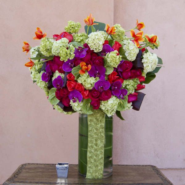 Bright mixed bouquet in a tall glass vase with pink, purple, and orange flowers.