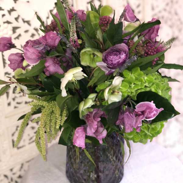 Purple and green mixed bouquet in a dark glass vase