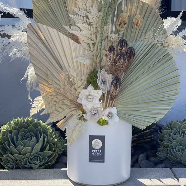 Tall arrangement with dried palm fans, white flowers, and pampas grass in a white vase.